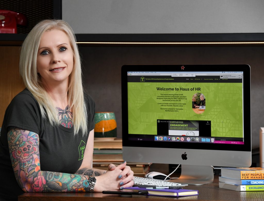 Person with blonde hair and tattoos standing next to a PC monitor